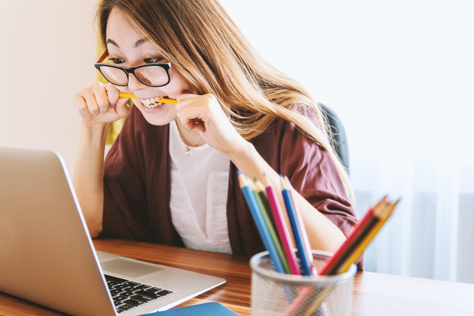 Una ragazza che morde una matita mentre lavora al computer