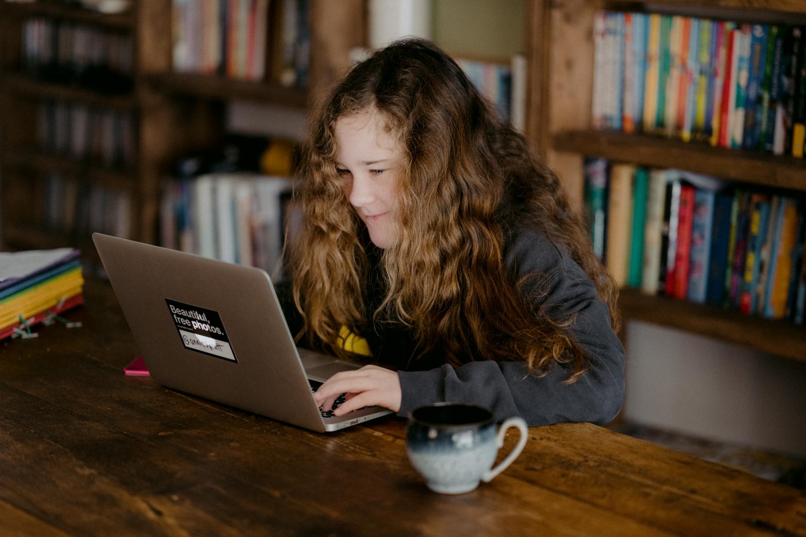 Ragazza che scrive su un computer, sullo sfondo una libreria