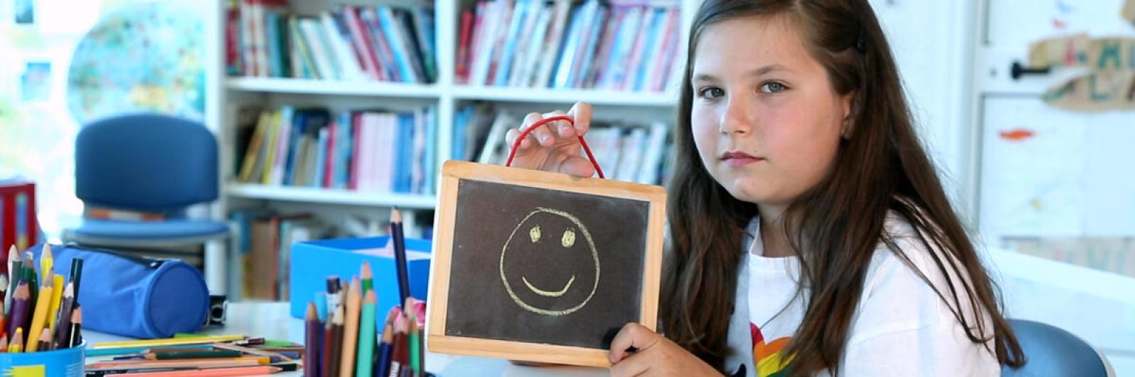 Bambina che tiene in mano un quadretto con un sorriso