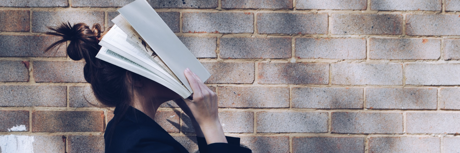 Una ragazza si copre il volto con un libro