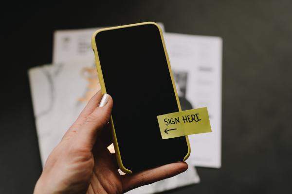 Telefono con un post it incollato che riporta la scritta "Signe here" (Firma qui)