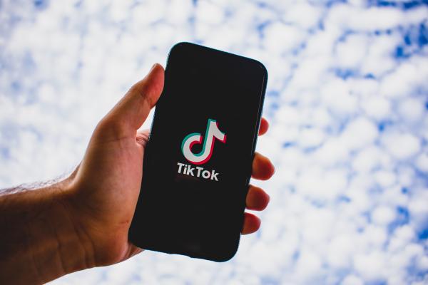 Una mano afferra uno smartphone, si vede l'app tik tok e sullo sfondo un cielo con le nuvole