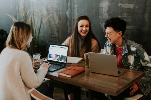 Ragazze sedute ad un tavolo con computer e libri, che ridono insieme