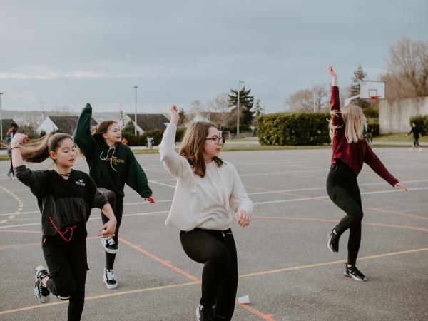 Quattro ragazze che ballano su un campo sportivo in asfalto.