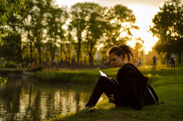 Ragazza seduta in riva ad un fiume che legge nella natura